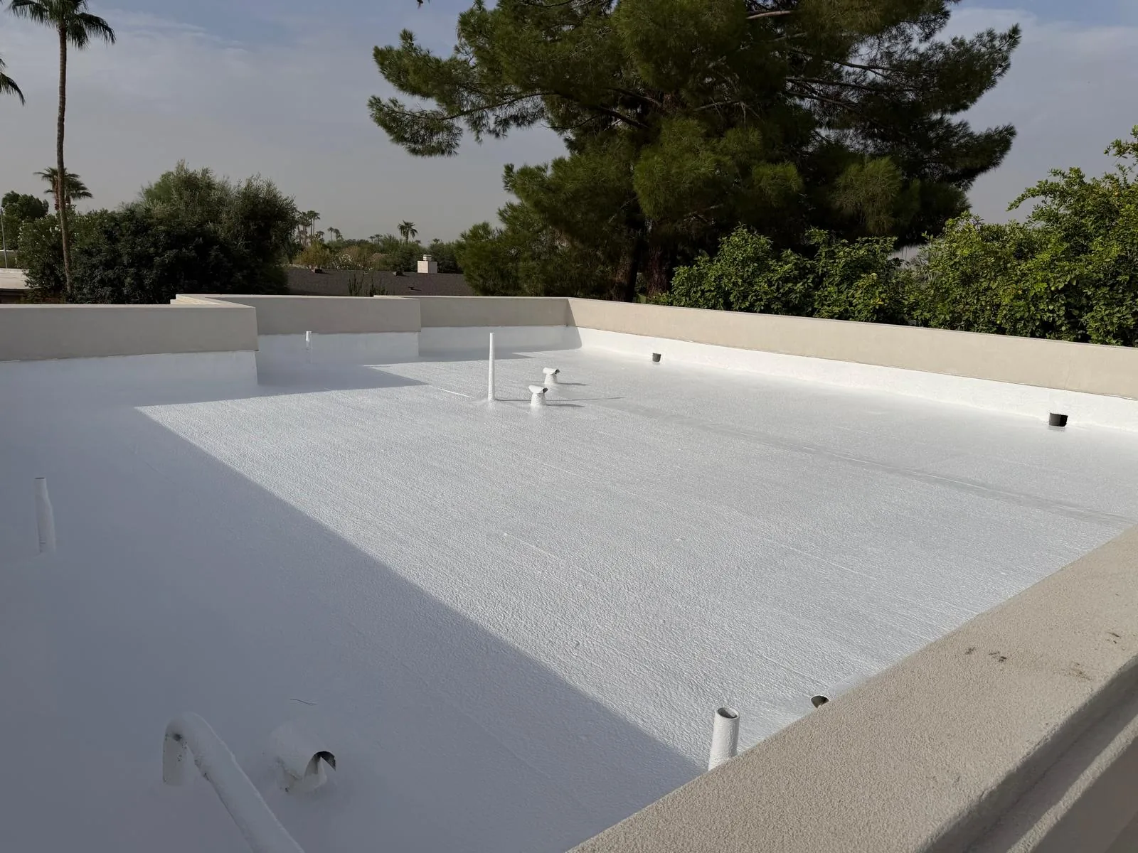 Flat roof finished in white elastomeric coating with parapet walls and new penetration seals